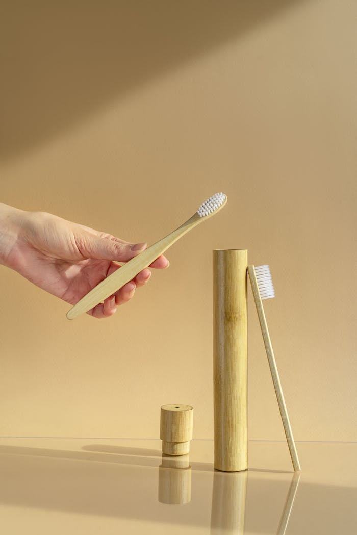 Hand holding a bamboo toothbrush with dental hygiene products on a beige background.